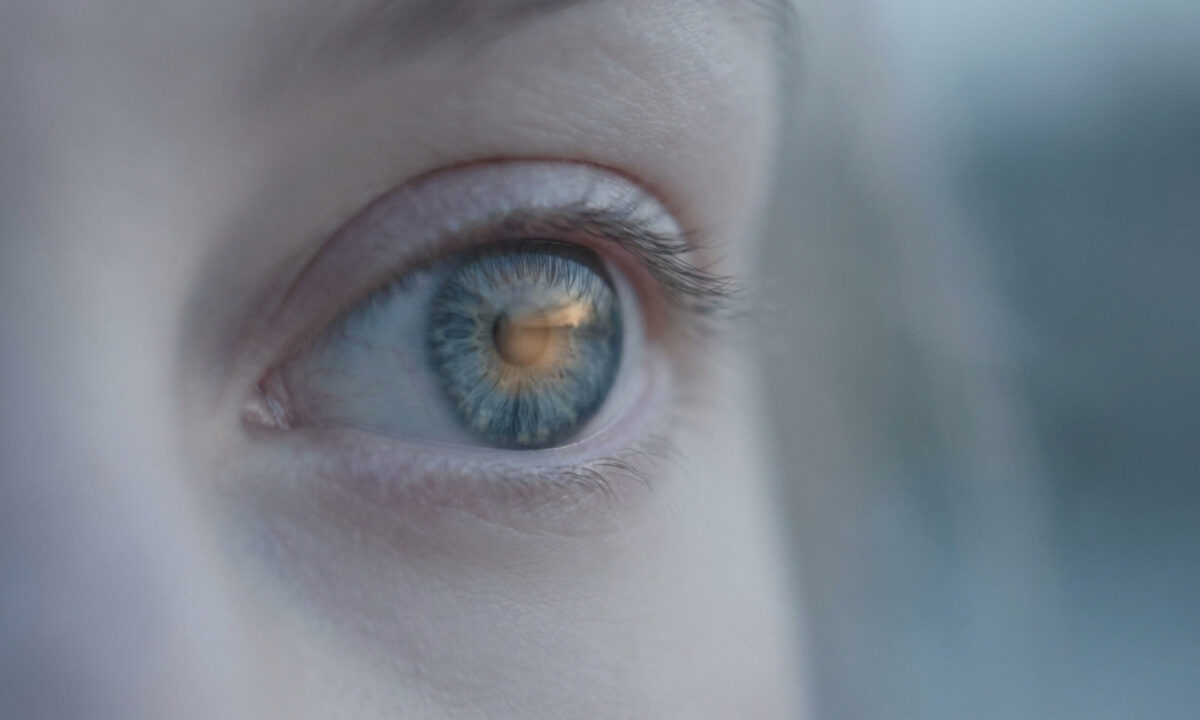 Gros plan sur un œil bleu clair reflétant une lumière chaude, symbolisant la vision et la santé.