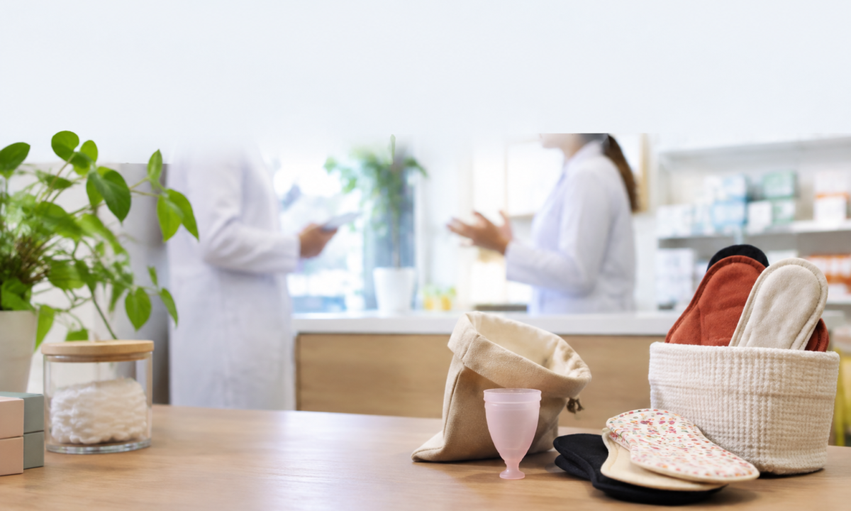 Protections périodiques réutilisables sur un comptoir de pharmacie avec du personnel flouté en arrière-plan.