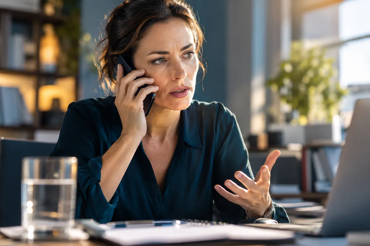 Une adulte appelle au téléphone près de son bureau, un verre d’eau en retrait.