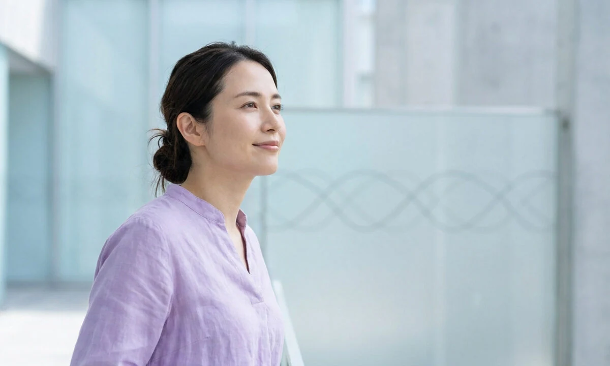 Portrait de profil d'une femme japonaise souriante portant un chemisier parme dans un environnement moderne et lumineux.